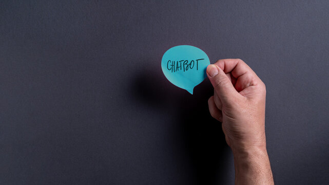 Hand holding a speech bubble with the word chatbot on a dark background in a modern setting