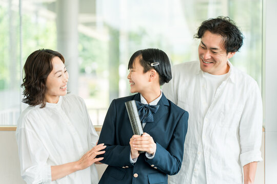 A middle school girl holding her graduation certificate and her parents