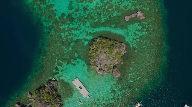 Drone rising top down shot ascending over a small limestone rock islet in clear turquoise sea in Coron, Palawan.