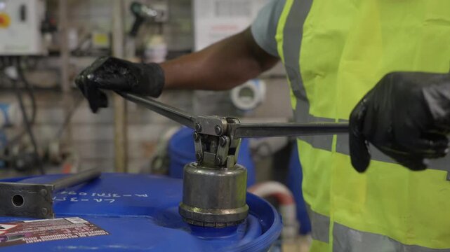 Worker in safety gear using drum tool on coolant barrel in industrial facility