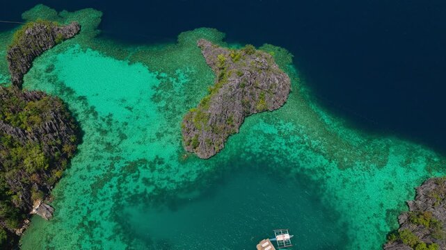 Aerial backwards top down view pulling away from a rocky coral reef islet in crystal clear ocean water in Coron, Palawan.