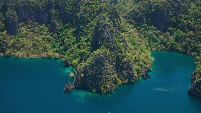 Aerial backward movement shot with a pan up revealing deep turquoise lagoons and limestone peaks in Coron, Palawan.