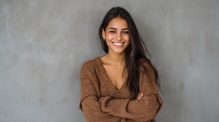 Fototapeta premium Portrait of a young latin woman with pleasant smile and crossed arms isolated on grey wall with copy space. Beautiful girl with folded arms looking at camera against grey wall. Cheerful hispanic woman