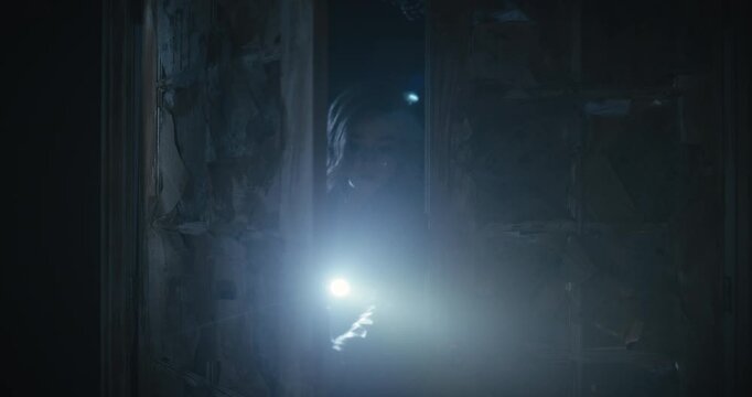 Curious woman with flashlight entering scary, shadowy room as she tries to prop door open behind her but it shuts anyways