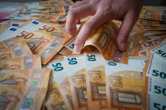Close-up of a hand grabbing 50 euro banknotes, representing taxes or greed