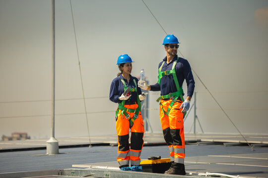 Maintenance team of technician and worker inspecting solar panels installation on industrial solar roof, Two solar engineers in safety uniform and harnesses working on rooftop solar farm