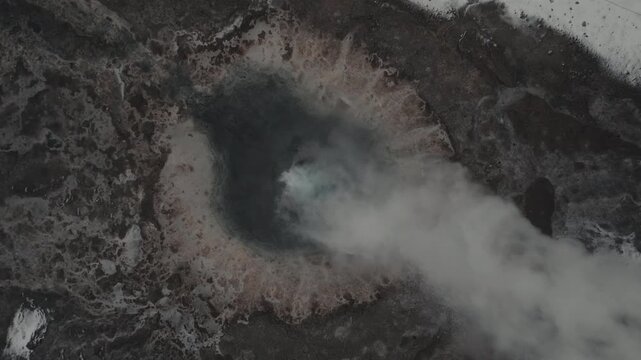 Top down aerial shot of a geyser erupting at the exact moment of explosion with steam and water bursting from the earth in a dramatic geothermal scene