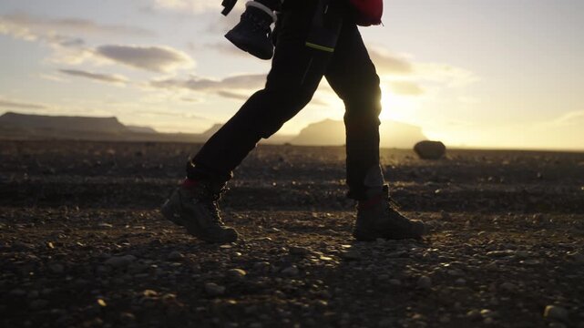 Super slow motion shot of legs walking over rocky terrain at sunrise with the sun backlighting the scene and creating a warm golden atmosphere in a remote landscape