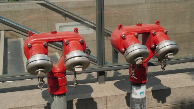 Two red industrial fire hydrants on city street against glass railing at sunny day.