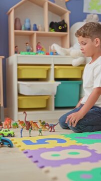 Boy kneels and reaches for a toy car and lines up dinosaur figures on a colorful number mat inside a building playroom; focused play.