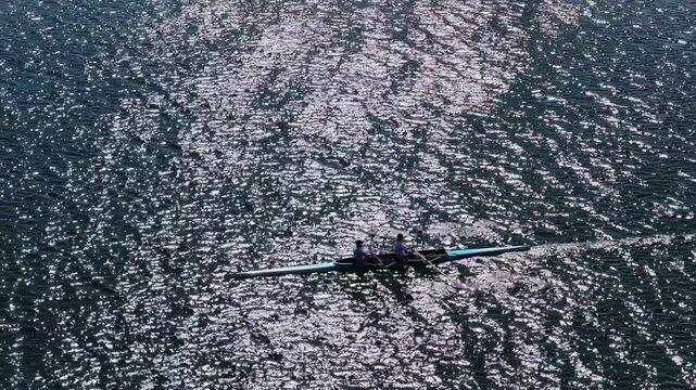 Drone shot of double rowing team paddling on sparkling water surface