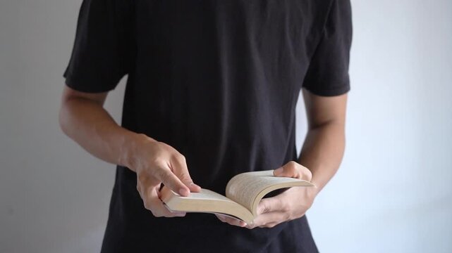 Man in Black Shirt Holding and Flipping Pages of Paperback Book
