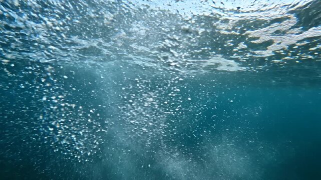 Underwater view of bubbles rising to the surface of clear blue water.