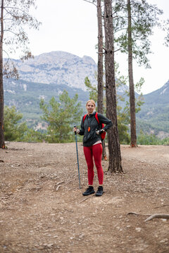 Woman with backpack and pole pauses on mountain trail