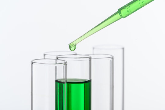 Laboratory dropper transferring green liquid sample into test tubes for chemistry research, pharmaceutical testing, and healthcare scientific experiments with copy space.