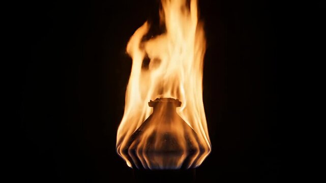 Closeup of a small vase engulfed in vibrant orange flames against a black background.
