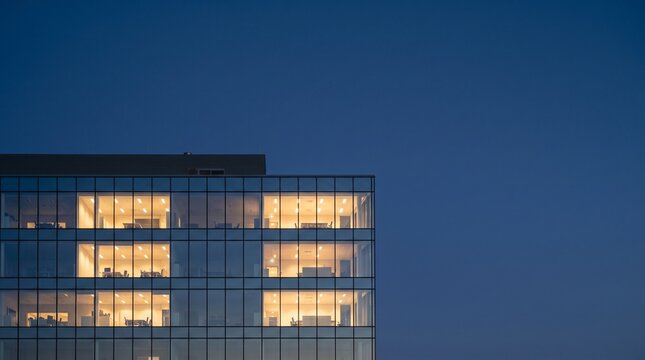 Modern office building facade illuminated at dusk with blue sky copy space.
