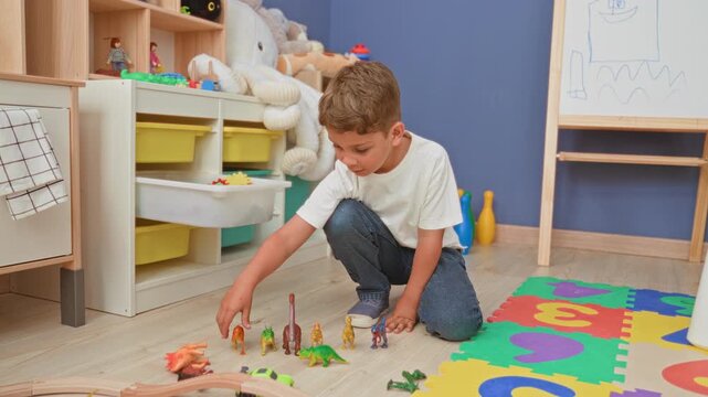 Boy arranging toy dinosaurs on the floor with his hand in a bright colorful playroom; playful imagination.