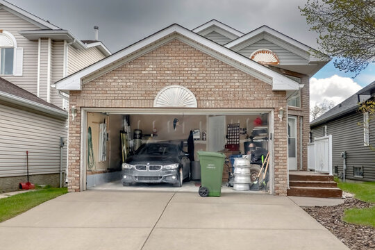 Calgary, Alberta, Canada. May 27, 2026. Straight-on view of an open residential garage featuring a parked BMW car and a green compost bin.