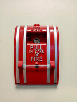 A red fire alarm pull station is mounted on a wall. It is used to alert for a fire in case of an emergency. This device is important for safety.