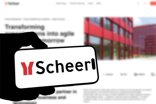 Kiel, Germany - 05-20-2026: Smartphone displaying the German IT consulting company Scheer app in the App Store in a workspace environment with laptop and notebook