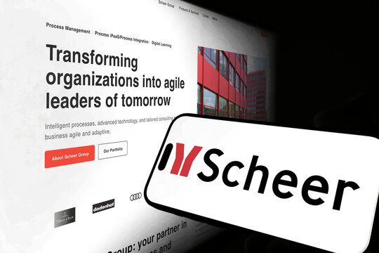 Kiel, Germany - 05-20-2026: Smartphone displaying the German IT consulting company Scheer app in the App Store in a workspace environment with laptop and notebook