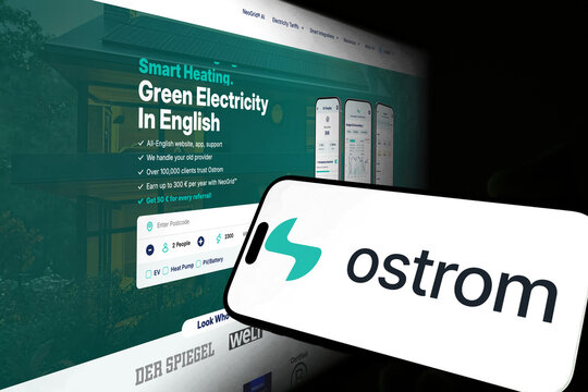Kiel, Germany - 05-20-2026: Smartphone displaying the German digital energy provider Ostrom app in the App Store in a workspace environment with laptop and notebook