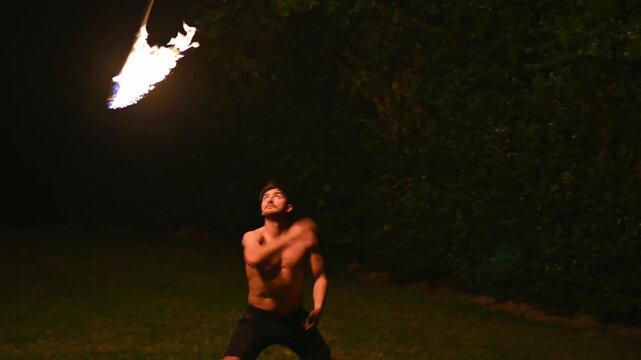 Young bare chested performer spinning fire staff at night