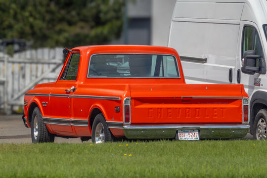 Calgary, Alberta, Canada. May 26, 2026. Rear three-quarter view of a vintage orange Chevrolet pickup truck parked behind a grass field.
