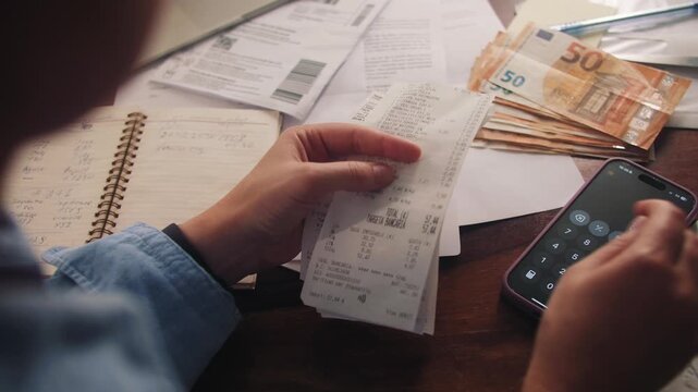 A woman calculates monthly expenses, for a period going through her purchase receipts and adding up on a calculator. Concept of a family budget. High quality 4k footage