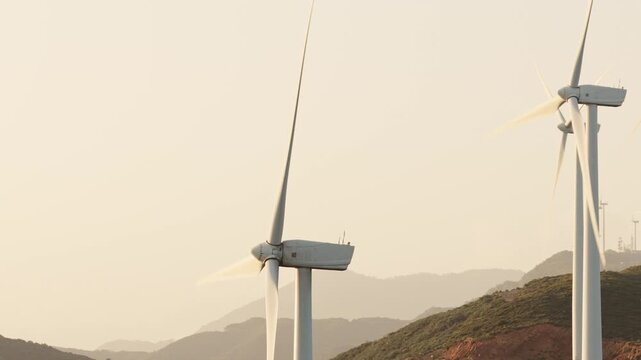 Windmills on a wind farm generating clean, renewable energy with their large propellers spinning against a background of mountains, producing sustainable electricity for a green future
