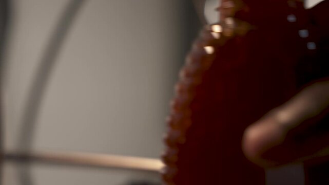 Rich amber honey streams into a textured plastic bottle, capturing the smooth flow and filling process. Suitable for food industry promotions or beekeeping documentaries.