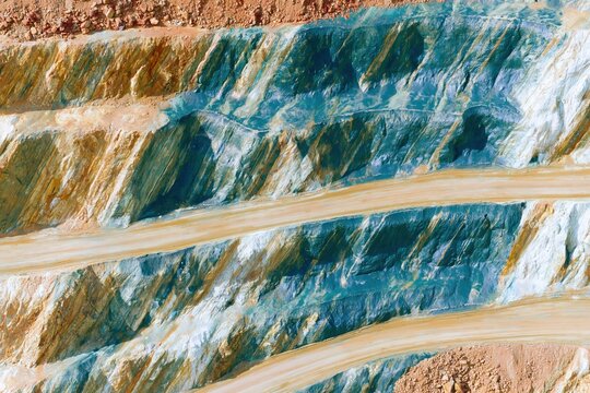 Open-pit mine excavation showing terraced earthwork levels with blue mineral deposits for industrial geology reports, mining industry websites and abstract backgrounds