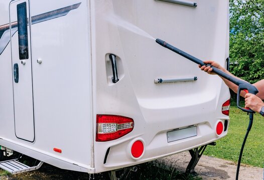 Washing a white RV motorhome with a high-pressure cleaner in a green outdoor setting