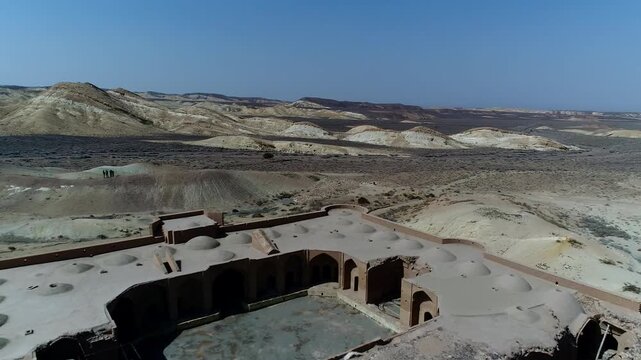 Close perspective of stone caravanserai ruins highlights thick walls and arched openings in desert setting under clear sky forming detailed historical architecture vista ideal for heritage stock