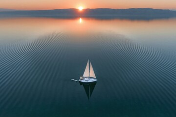 Fototapeta premium Calm sea surface with sailboat and paddleboarders at sunset for travel brochures, luxury lifestyle advertising and marine tourism background with distant mountains