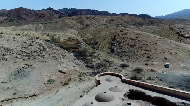 Curved stone wall detail of caravanserai ruins stands against desert mountains under clear blue sky forming architectural historical feature vista ideal for heritage and archaeology stock video