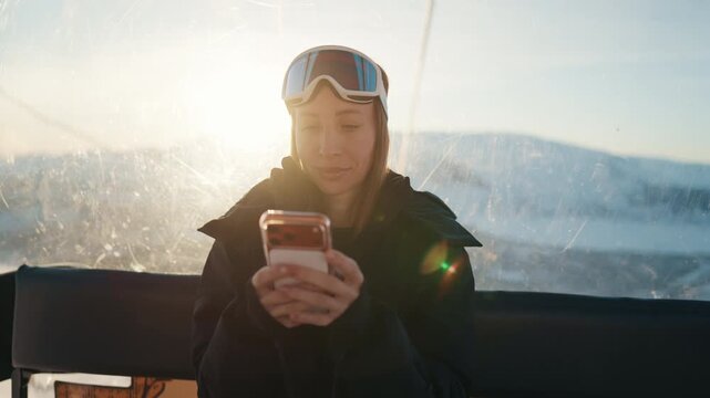 Woman tourist riding cable car in ski resort and using modern smartphone. Internet addiction of modern people, travel blogger online, female tourist surfing internet in roaming, use mobile app