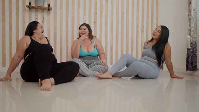A group of three plus-size girls in a room were sitting and chatting happily after exercising together.