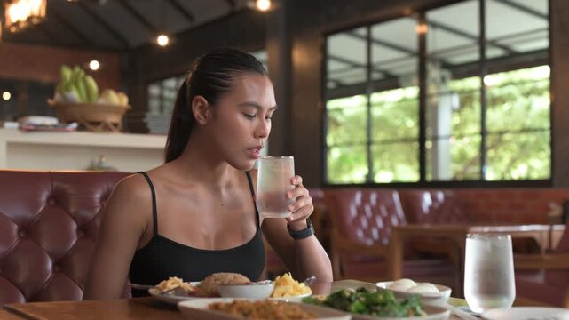 Thai woman drinking water and looking away with traditional Thai food in restaurant horizontal shot