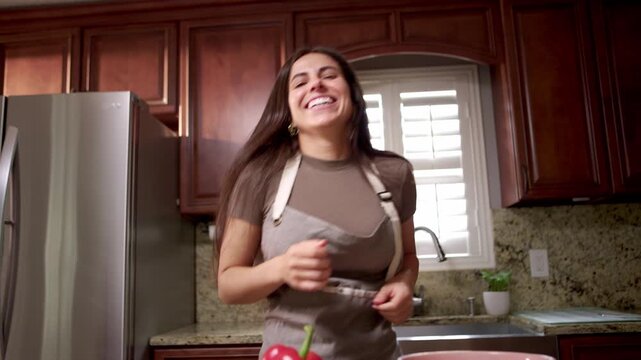 Woman looks at camera and dances while cooking