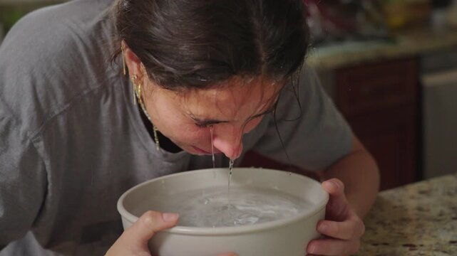 Woman dunks face into ice water as part of skin care routine.