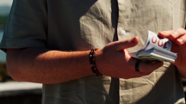 Close-up shot of a man holding a thick stack of US dollar bills in warm sunlight outdoors. Finance, wealth, cash flow, spending, success, lifestyle, business and money concept.