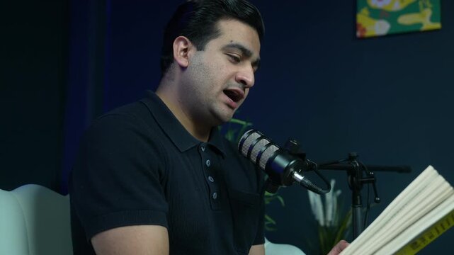 Male narrator holding an open book and speaking into a professional microphone during a studio recording session. Ideal for audiobook, storytelling, and digital literature concepts