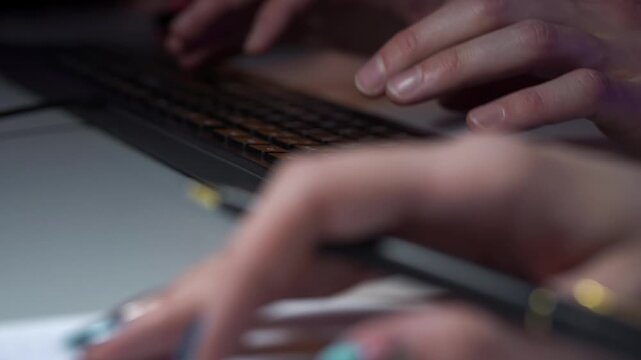 Closeup hands writing code notes on notebook during pair programming session beside monitors, pen sketching flowcharts and algorithm steps, dim blue ambient lighting and blurred collaborator