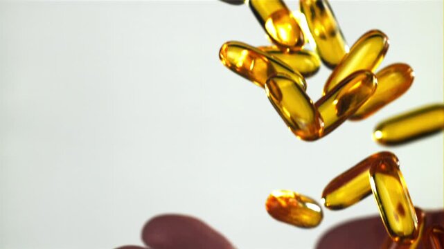 Golden softgel capsules falling into open hand under warm light Filmed on a high-speed camera at 1000 fps.