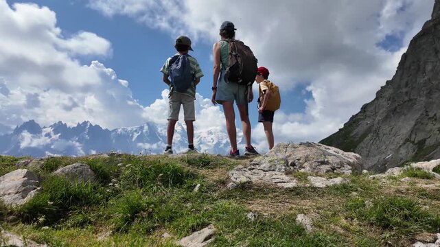 Adventurous mother hiking with two children in the alps, admiring the majestic mont blanc mountain range from a panoramic viewpoint in summer, with the camera moving away