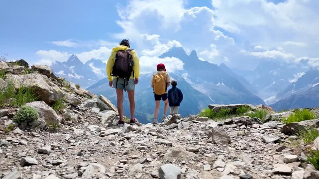 Mother and two children hiking on a mountain path in the alps, walking towards a breathtaking view of the mont blanc massif with its stunning glaciers and peaks