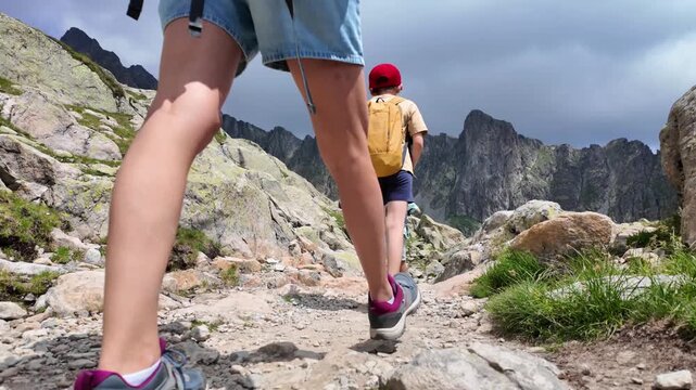 Mother and children hiking on a rocky mountain trail, family trekking adventure in a breathtaking alpine landscape with dramatic cloudy sky, exploring nature during summer vacation