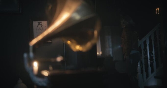 Working gramophone in dark, creepy home as woman with flashlight quickly turns around to see it - medium shot
